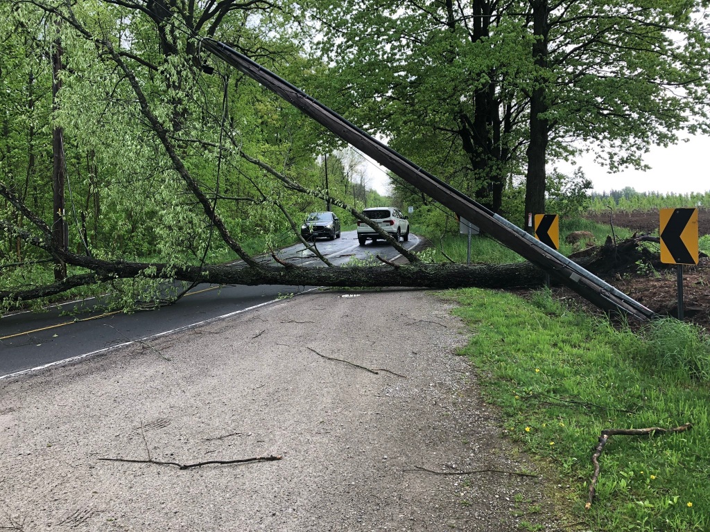 Storm damage from May 21, 2022 derecho showing a hydro pole and tree over a two lane road.